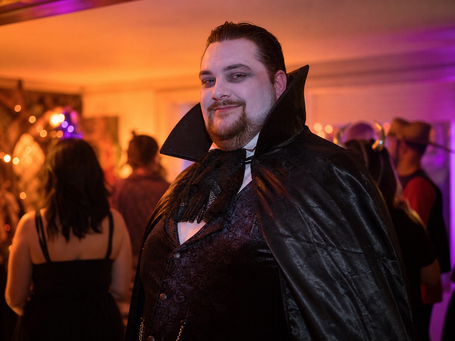 A plus size man wearing a dramatic vampire-style Halloween costume at an indoor party