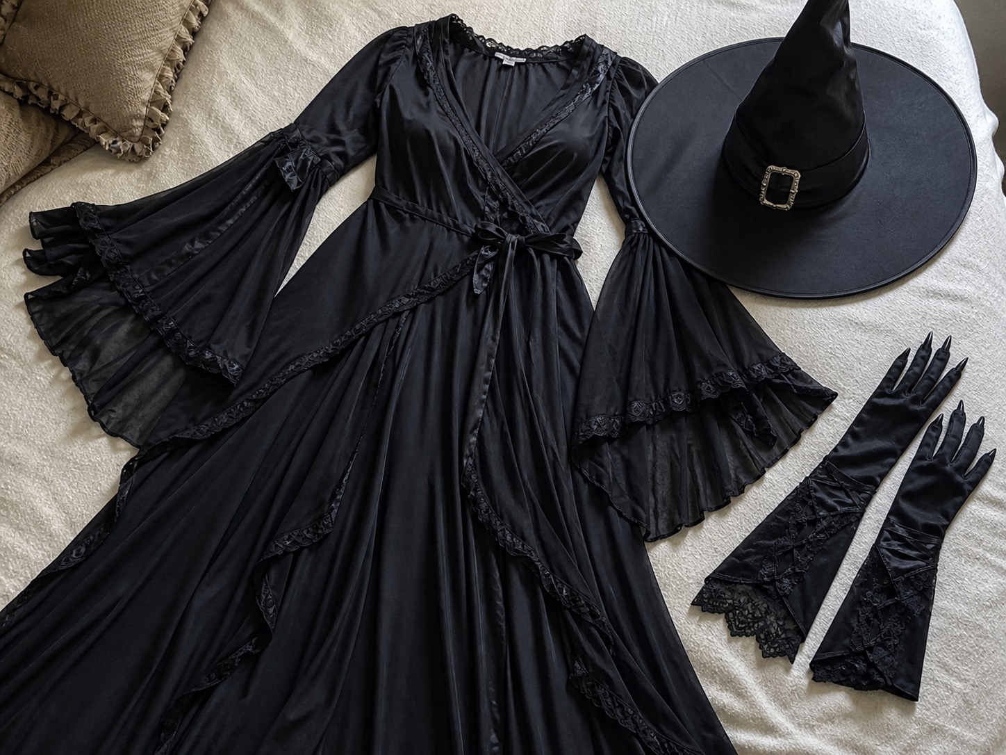 Plus size Halloween costume pieces including a witch-style dress, pointed hat and dramatic gloves laid out on a bed