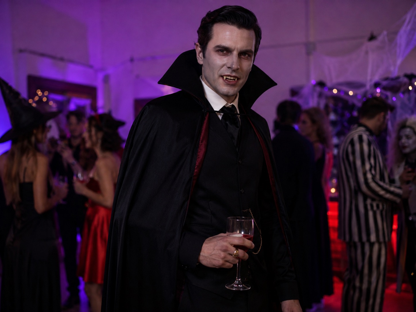 Man wearing a dark suit, full-length black cape and visible fangs at a Halloween party