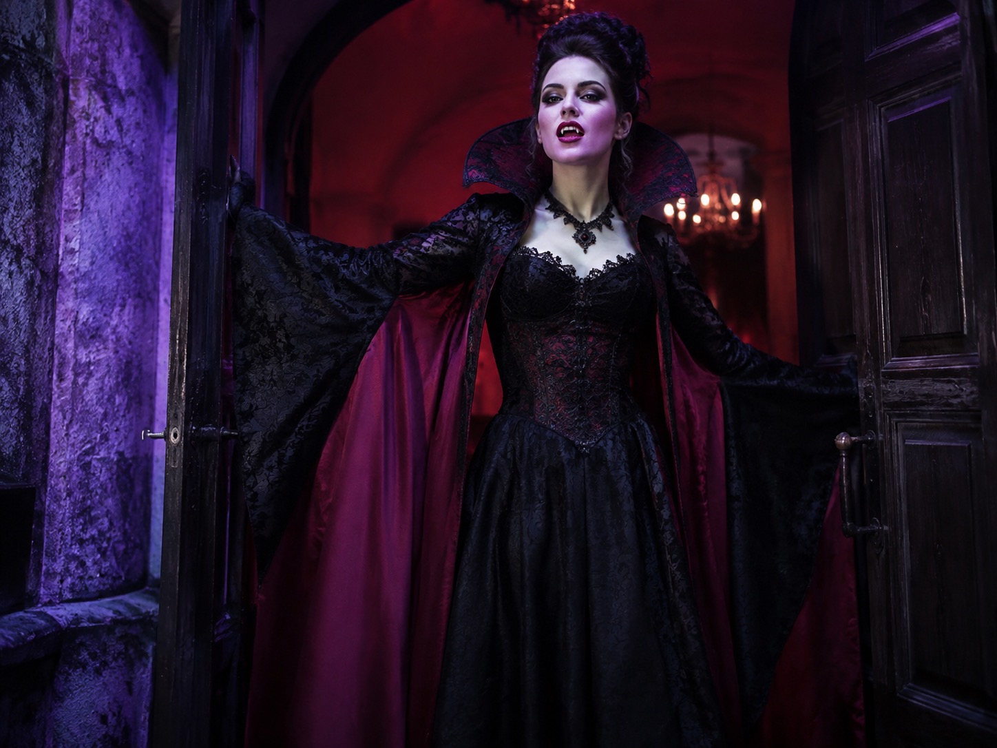 Woman wearing a dramatic gothic vampire costume with a cape and theatrical makeup