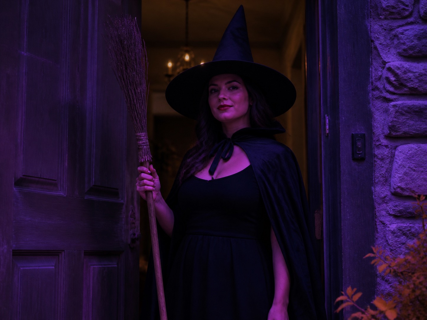 A woman wearing a classic witch costume with a pointed hat, cape and broom prop